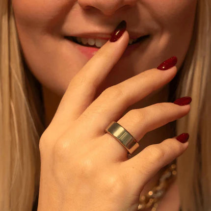 Close-up of a hand with a gold ring and red nail polish, with a blurred background.