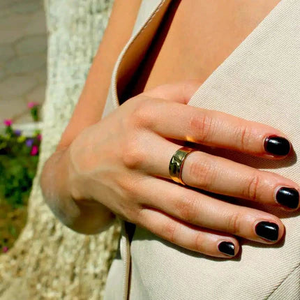 Hand with black nail polish wearing a gold ring against a blurred background
