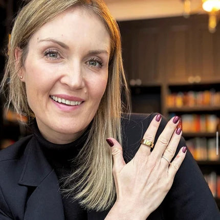 Woman with a smile, showing her hand with purple nail polish and rings.