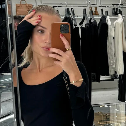 Woman taking a mirror selfie in a clothing store holding a phone with a brown case.