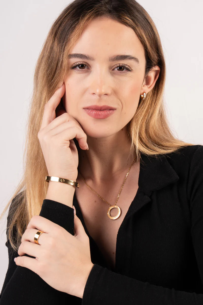 Woman wearing gold jewelry including a necklace, bracelet, and ring on a plain background