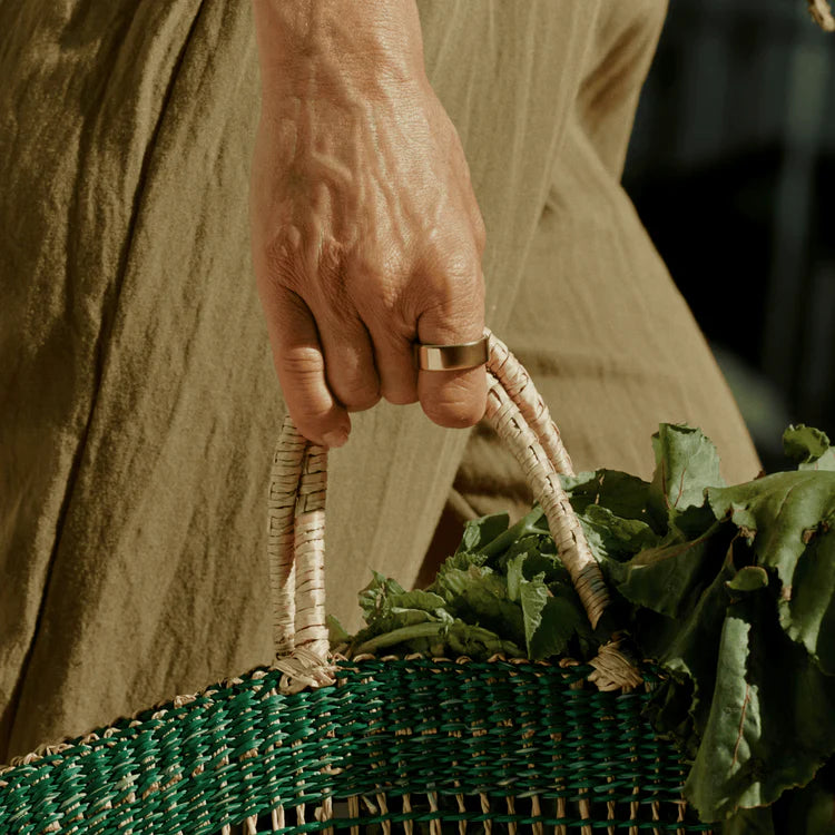 Person holding a green woven basket filled with leafy greens.